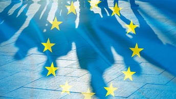 Auf einer Unterfläche mit Fliesen ist der bläuliche Schatten von mehreren Personen. Über der Mitte ist ein Kreis, bestehend aus goldenen Sternen