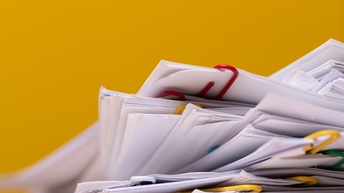 Detailansicht ungeordneter Dokumenten mit Büroklammern zusammengefasst auf gelbem Hintergrund