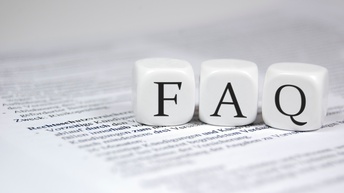 Drei weiße Würfel liegen nebeneinander auf einem bedruckten Papier. Auf dem linken Würfel ist ein f, dann folgt ein a und dann ein q