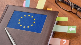 Notizbuch mit im Kreis verlaufenden gelben Sternen auf blauem Hintergrund am Cover hat in den Seiten eingeklebte Streifen, daneben liegt eine Brille, auf dem Notizbuch liegt ein Kugelschreiber