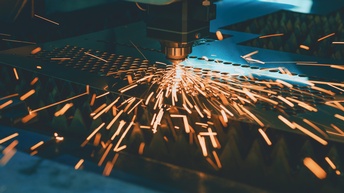 Nahaufnahme eines Lasers, der in eine dünne Metallplatte Löcher lasert