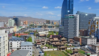 Stadtansicht von Ulan Bator: Blick auf den Choijin Lama Tempel mit Kloster in der Mongolei. Daneben moderne Wolkenkratzer, Berge im Hintergrund unter blauem Himmel.