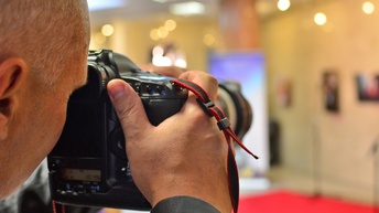 Rückenansicht und Nahaufnahme einer Person, die mit einer Kamera fotografiert. Im Hintergrund ist ein roter Teppich in einem Raum