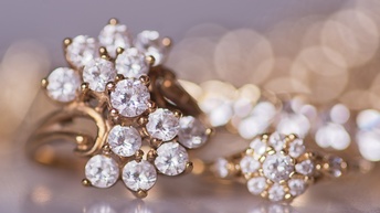 Nahaufnahme von einem Goldschmuckstück mit Juwelen besetzt, dahinter zeigt sich in Unschärfe ein helles Bokeh