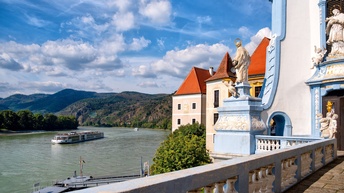 Blick vom Stift Dürnstein mit architektonischen Details des Stiftes auf die Donau, bewaldete Hügel im Hintergrund, am Fluss ein Schiff