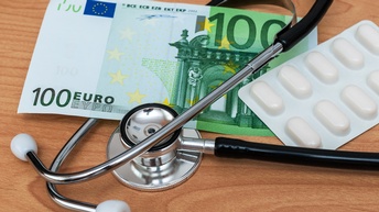 Ein Stethoskop liegt mit einem 100-Euro-Schein und einer vollen Tablettenverpackung auf dem Tisch.