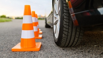 Nahaufnahme dreier nebeneinander stehender Verkehrshütchen, die neben einem PKW stehen