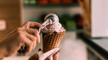 Eine Hand füllt mit einem Eiskugelportionierer Speiseeis in ein Hörnchen