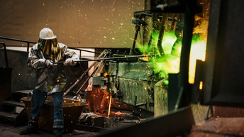 Person in Schutzkleidung hält Stange in Industrieanlage, aus der grünes Licht und Funken treten