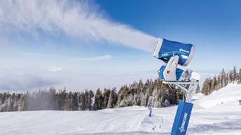 Schneekanone auf verschneiter Skipiste vor Waldkulisse