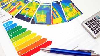 Eine Energieeffizienzskala, Infrarot Wärmebilder von Häusern sowie ein Taschenrechner und ein Kugelschreiber auf einem Tisch