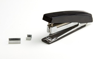 Ein Heftklammern-Tacker vor einem weißen Hintergrund. Neben dem Tacker liegen Heftklammern