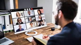 Person vor Computer sitzend, mehrere lächelnde Personen am Bildschirm