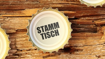 Kronkorken mit der Aufschrift Stammtisch auf morschem Holz liegend, ringsum weitere Kronkorken im Ausschnitt