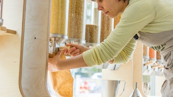 Person in Schürze beugt sich zu Getreidedispensern und befüllt Papiertüte