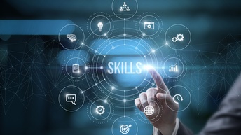 Hand einer Person in Businesskleidung zeigt mit einem Finger auf Grafik mit Schriftzug Skills als Konzept von Fähigkeiten, daneben sind mehrere Icons zum Thema kreisförmig vor einem dunklen Hintergrund angeordnet