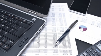 Büroalltag mit Laptop, Smartphone, Taschenrechner, Kugelschreiber und Finanzdokumenten