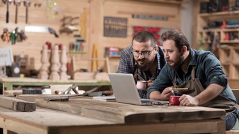 Zwei Tischler in Werkstatt vor Laptop sitzend