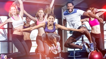 Frontalaufnahme von sechs verschiedenen Personen in Sportkleidung, die alle in die Luft springen. Im Hintergrund sind verschiedene Sportgeräte