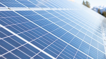 Leicht schräg stehende Solarkollektoren. Im Hintergrund sind grüne Bäume und eine Bergkette