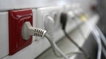 Nahaufnahme einer roten Steckdose, im Hintergrund sind weitere Steckdosen mit angeschlossenen Steckern