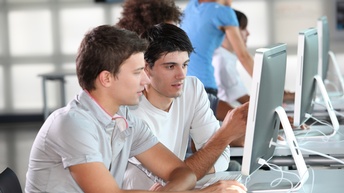 Zwei Personen sitzen vor Computerbildschirm