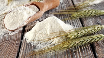 Nahaufnahme von fein gemahlenem Mehl und Ähren, die auf einem Holztisch liegen