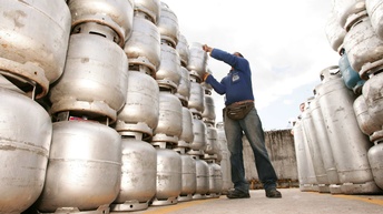 Viele, hellgraue Metallfässer sind übereinander gestapelt. Daneben steht eine Person, die ein Fass herunterhebt
