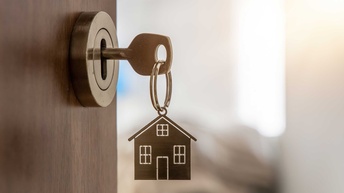 Eine geöffnete Tür mit einem Schlüssel mit einem Anhänger in Form eines Hauses im Türschloss