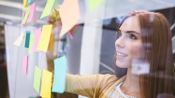 Lächelnde Person beschriftet mehrfarbige auf durchsichtiger Wand klebende Post-Its
