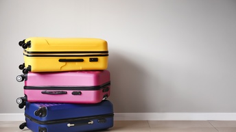 Drei Rollkoffer in den Farben Gelb, Pink und Blau aufeinandergestapelt