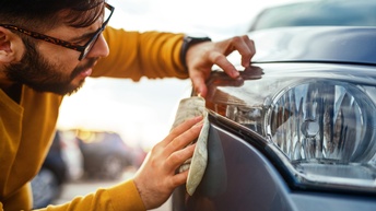 Person mit dunklen kurzen Haaren und Brille poliert das vordere Licht eines Autos