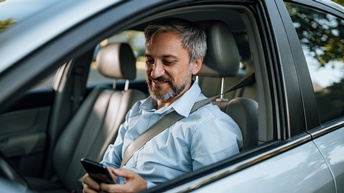 Lächelnde Person auf Fahrersitz eines Pkws blickt auf Smartphone