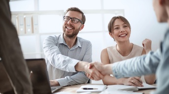 Personen an einem Besprechungstisch geben sich freudig die Hände