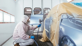 Person lackiert eine Fahrzeugkarosserie mit einer Sprühpistole