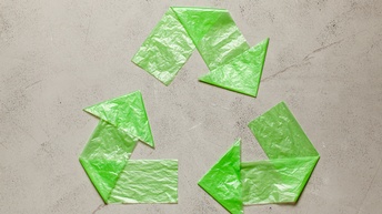 Ein aus grüner Plastikfolie gestaltetes Recycling-Symbol auf beigem Hintergrund: Drei im Kreis verlaufende Pfeile.