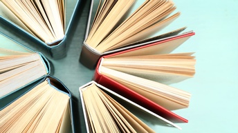 Aufnahme mehrerer Bücher, die auf einem hellen Untergrund stehen und teilweise aufgeklappt sind