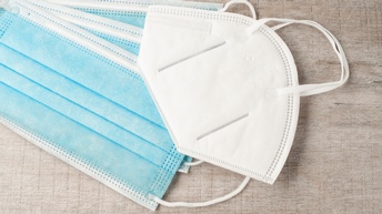 Blaue Mund-Nasen-Schutzmasken sowie eine FFP2-Maske vor einem Holzuntergrund