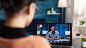 Person in Rückenansicht sitzt vor aufgeklapptem Laptop auf dessen Monitor weitere Person zu sehen ist