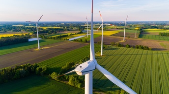 Fokus auf Windrad mit rotweißroten Spitzen auf Feld mit weiteren Windrändern stehend unter blauem Himmel