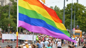 Regenbogenfahnen im Wind wehend im Hintergrund verschwommen große Menschengruppe auf Straße