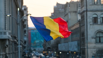 Die rumänische Flagge weht im Wind, im Hintergrund eine Stadtansicht.