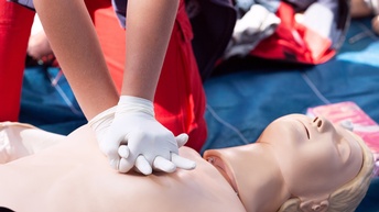 Erste Hilfe Training mit einer Puppe, eine Hand mit weißen Handschuhen führt eine Herzdruckmassage durch