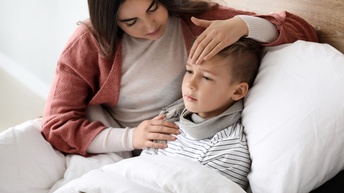Erwachsene Person mit langen dunklen Haaren kümmert sich um ein krankes Kind im Bett
