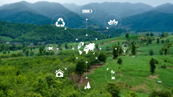 Im Vordergrund sind in einem Kreis verschiedene Symbole angeordnet wie eine Glühbirne, ein Stecker, ein Akku, eine Pflanze, ein Haus oder Bäume. Im Hintergrund ist eine grüne, bergige Landschaft