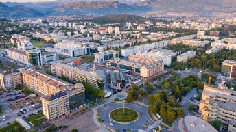 Stadtansicht von Podgorica: Häuserblocks, begrünter Kreisverkehr, im Hintergrund Bergkette