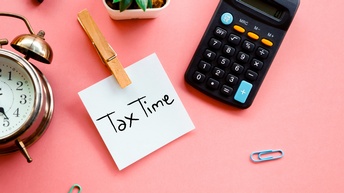 Bildkonzept mit Post-It Tax Time, daneben liegen ein Taschenrechner, eine Zierpflanze, ein Wecker sowie Büroklammern auf einem rosaroten Hintergrund