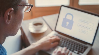Person mit Brille im Fokus arbeitet an einem Laptop und versucht sich mit einem Passwort einzuloggen
