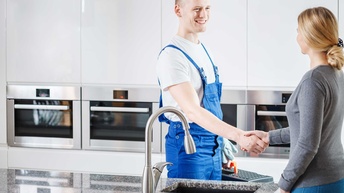 Ein Sanitärtechniker steht mit einer Kundin in einer Küche