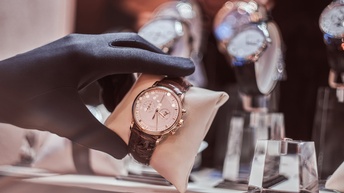 Hand mit schwarzen Handschuh hält eine Uhr in einem Juweliergeschäft